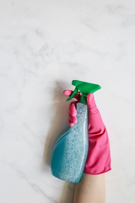 Des mains gantées nettoient les poignées d’un meuble avec un spray et un chiffon pour garantir l’hygiène.